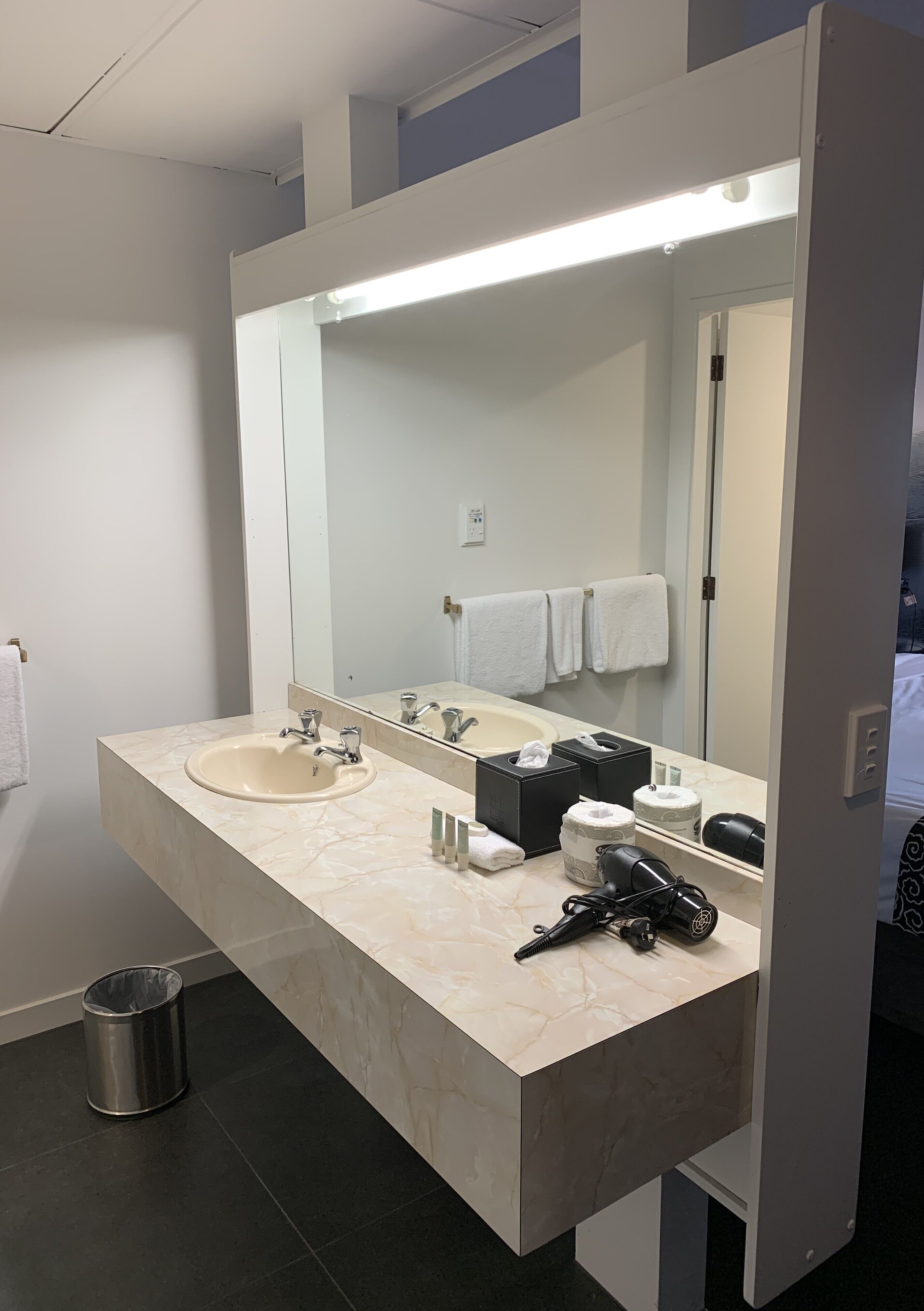 Une salle de bain moderne avec un lavabo en marbre, un grand miroir et un sèche-cheveux posé sur le comptoir.
