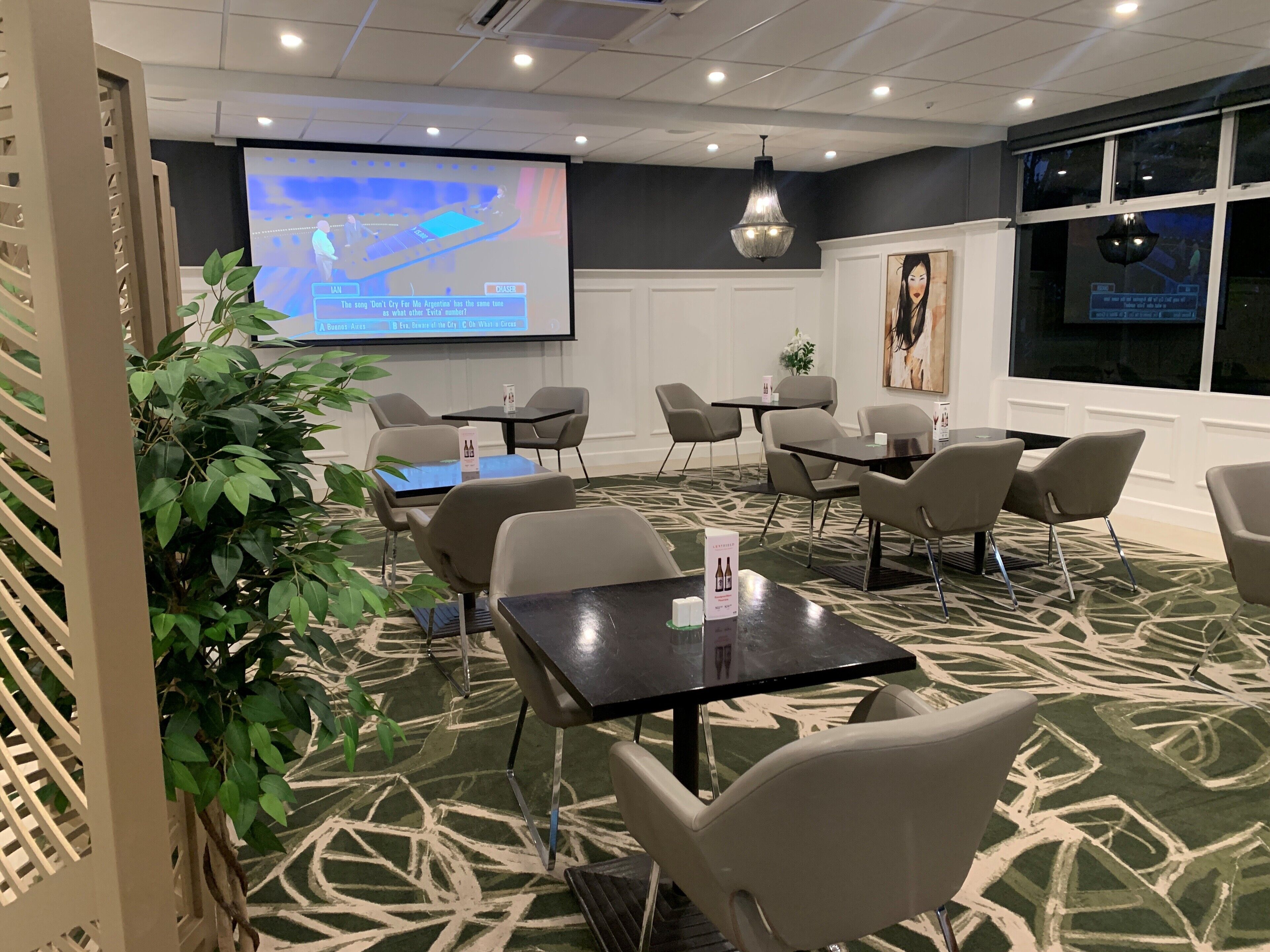 A conference room with a projector screen displaying a quiz, several tables and chairs, and a decorative plant.