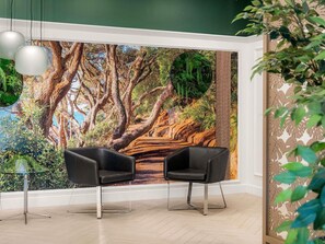 A room with two black chairs, a glass table, and a mural of a forest scene. - Mercure Tauranga (Tauranga)
