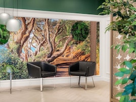 Una habitación con dos sillas negras, una mesa de vidrio y un mural con una escena de bosque.