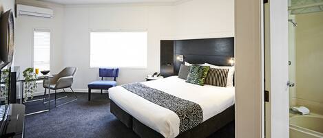 A hotel room with a bed, a desk, a chair, a window, and a shower area.