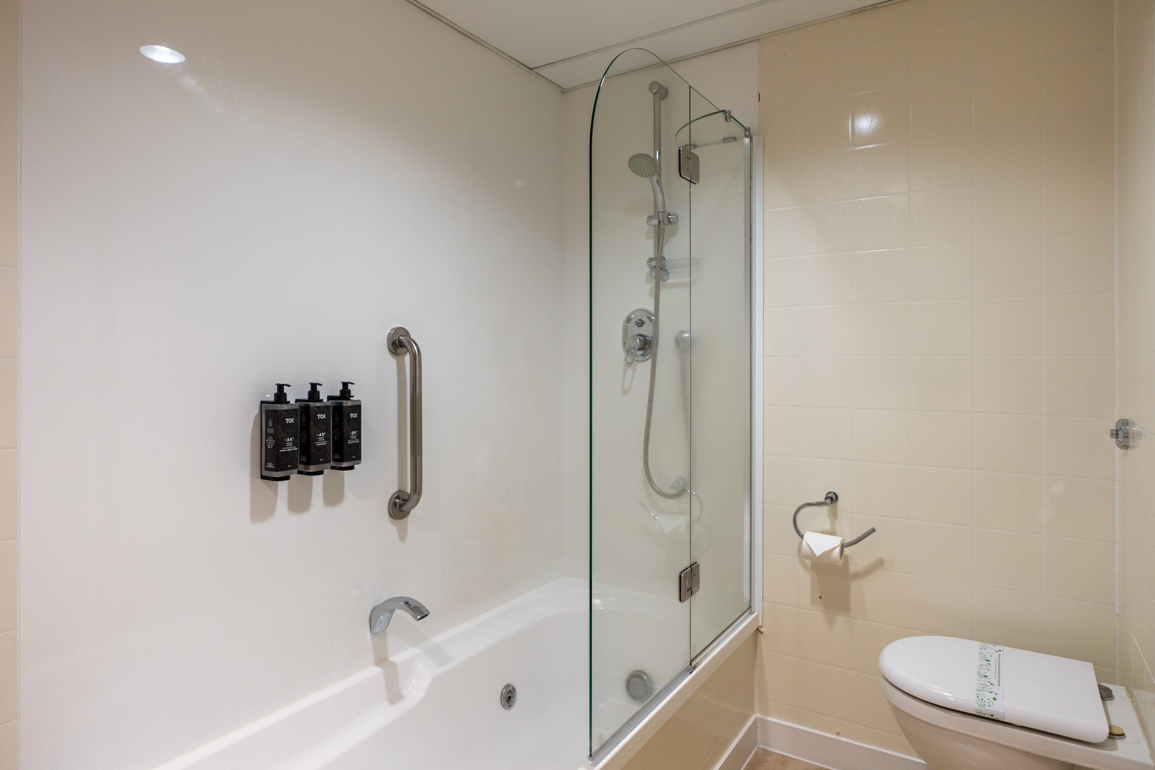 A modern bathroom with a glass-enclosed shower, a white bathtub, and a toilet.