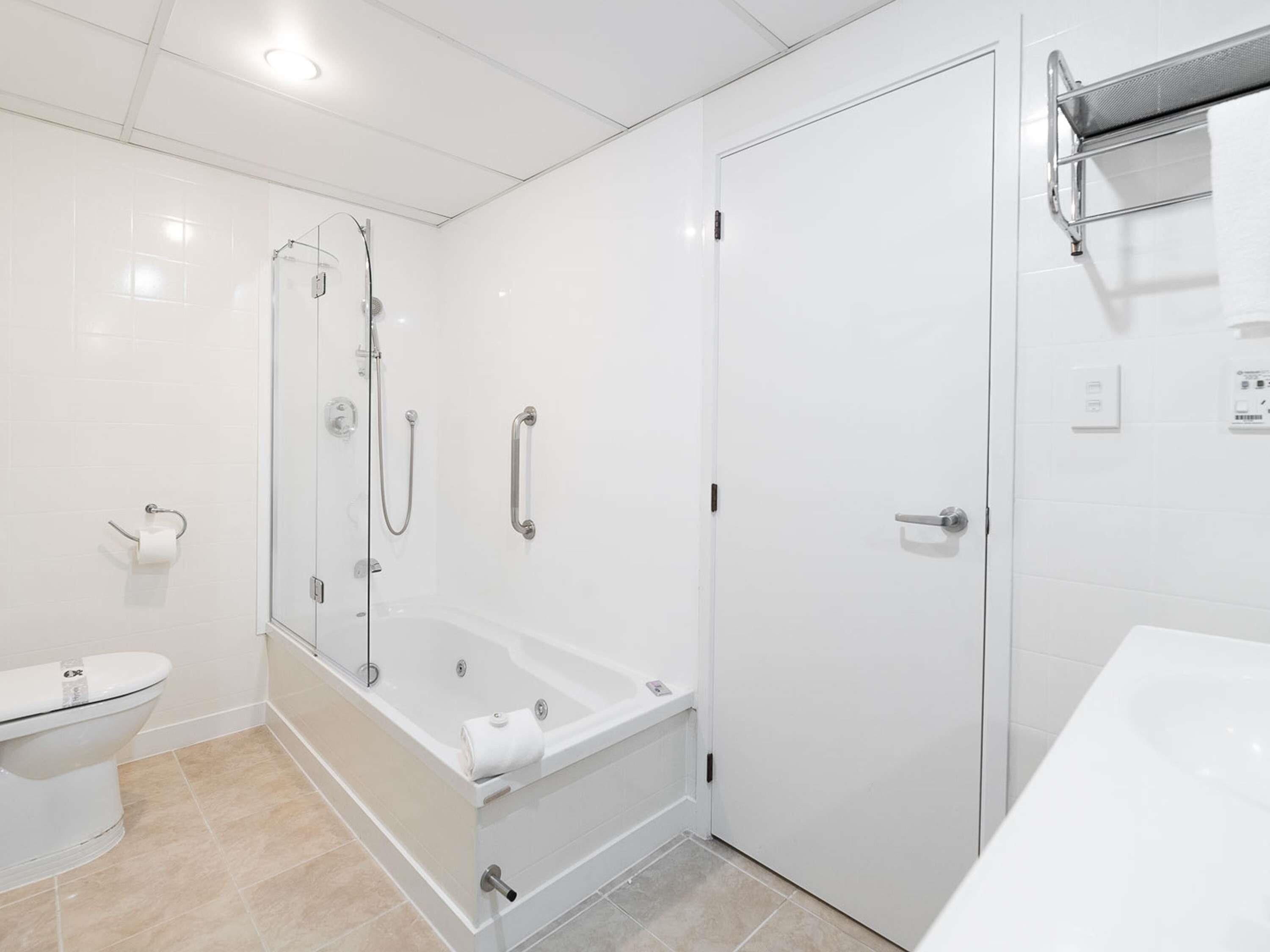 A modern bathroom with a glass-enclosed shower, a white bathtub, and a toilet.