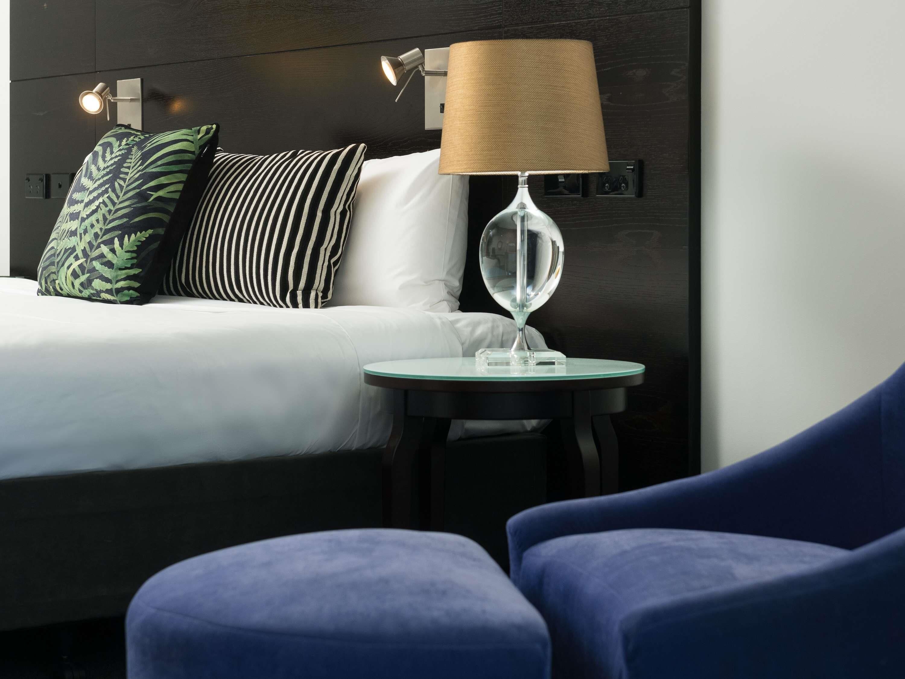 Une chambre d’hôtel avec un lit, une lampe de chevet, une petite table et deux fauteuils.