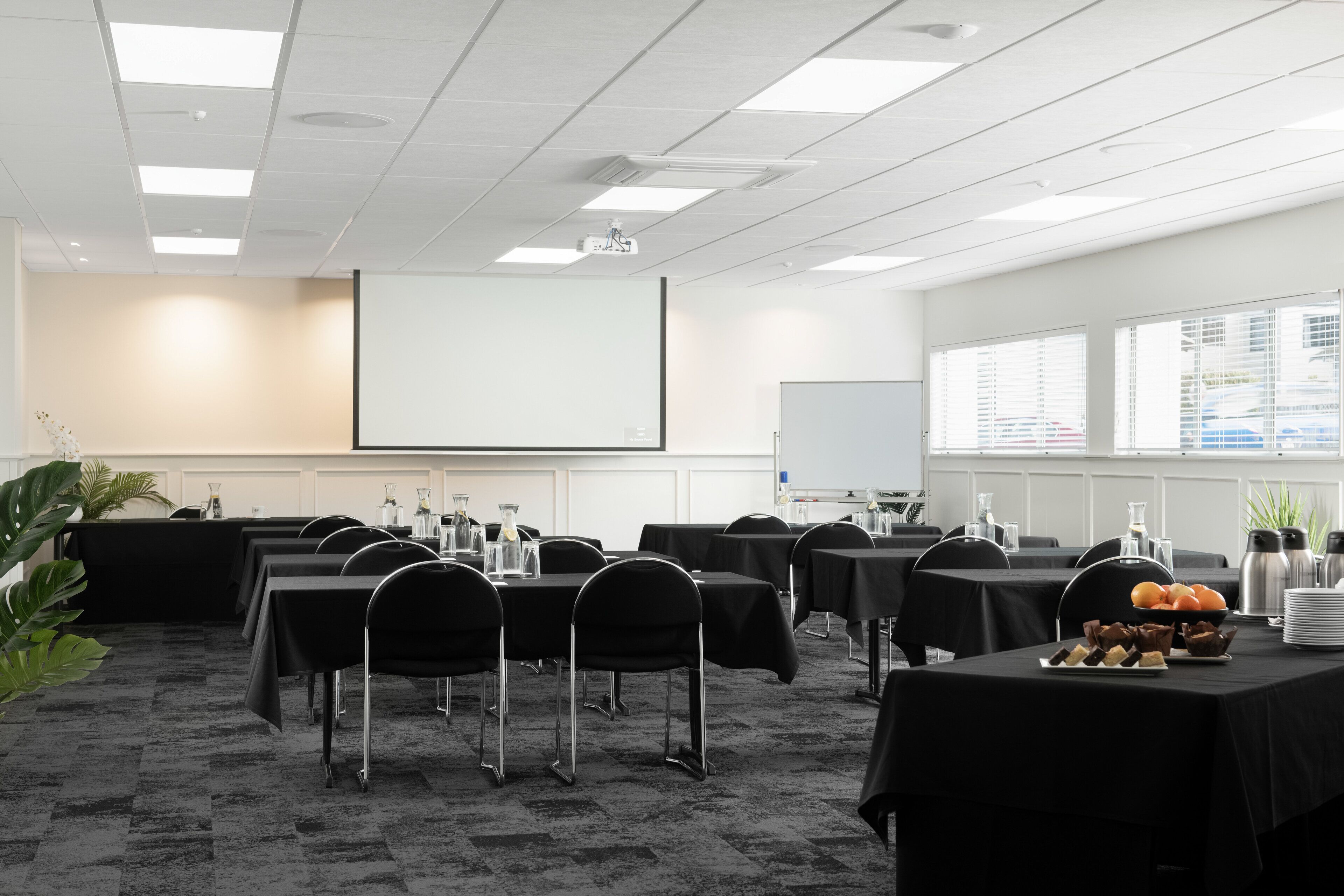 A conference room with tables, chairs, a projector screen, and a whiteboard.