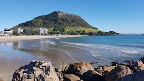 A beach with rocky foreground, a sandy shore, and a mountain in the background. - Mercure Tauranga (Tauranga)