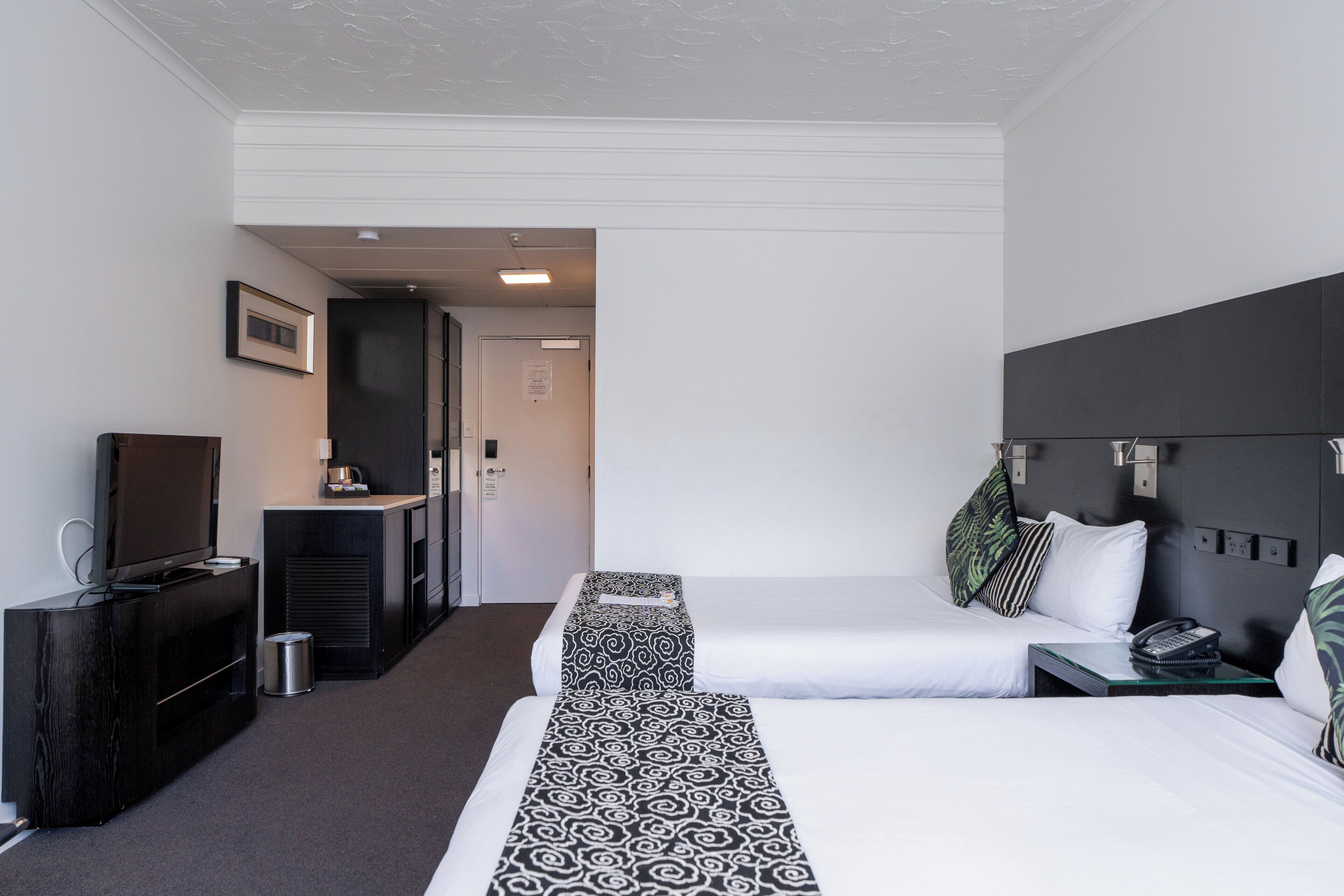 Een hotelkamer met twee bedden, een televisie, een bureau met telefoon en een kleine prullenbak.