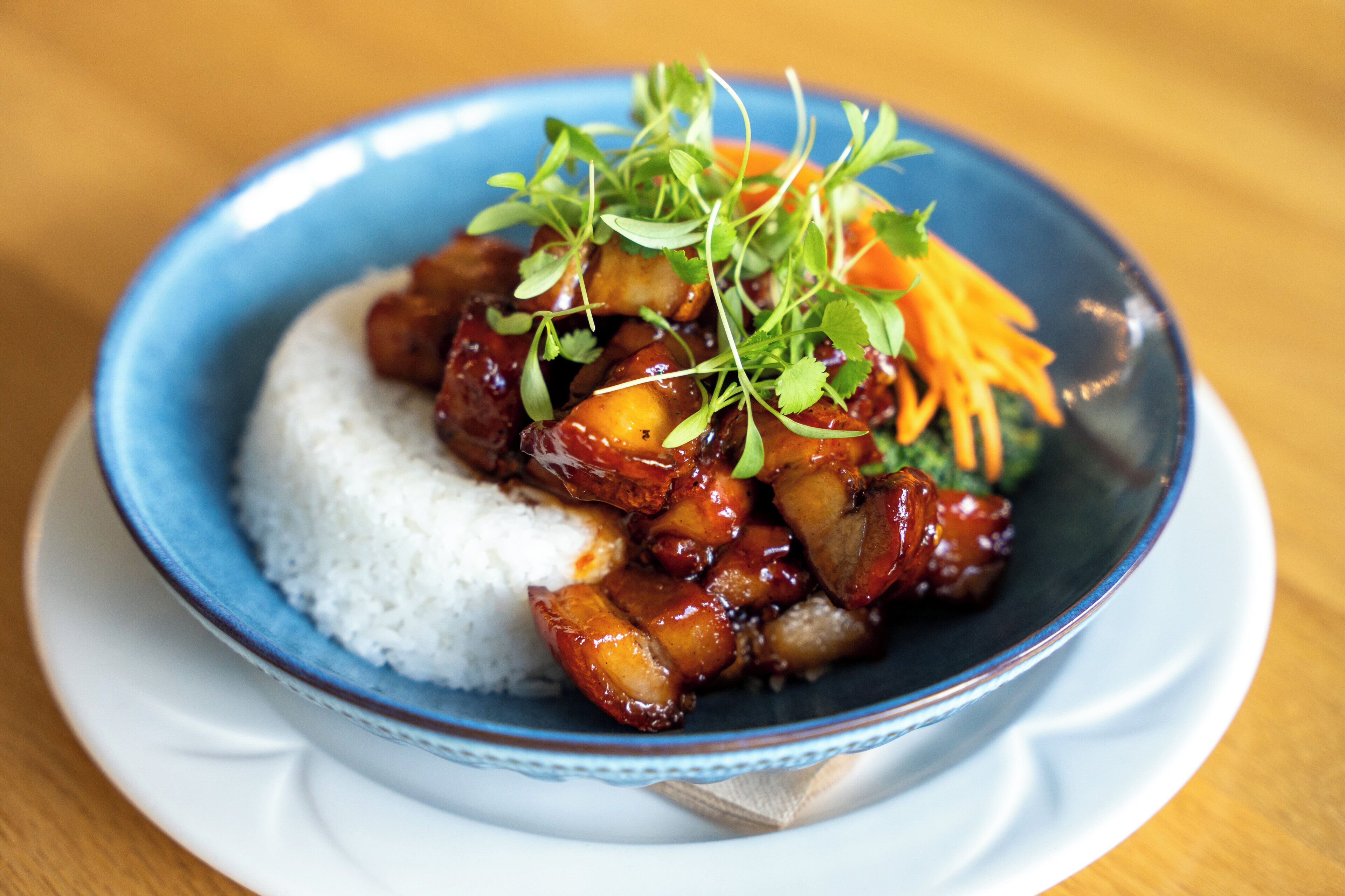A bowl of white rice topped with glazed meat and garnished with green herbs.