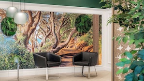 A room with a large mural of a forest scene, two black chairs, a glass table, and hanging pendant lights. - Mercure Tauranga (Tauranga)