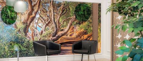 Habitación con un mural grande de un paisaje forestal, dos sillas negras, una mesa de vidrio y lámparas colgantes.