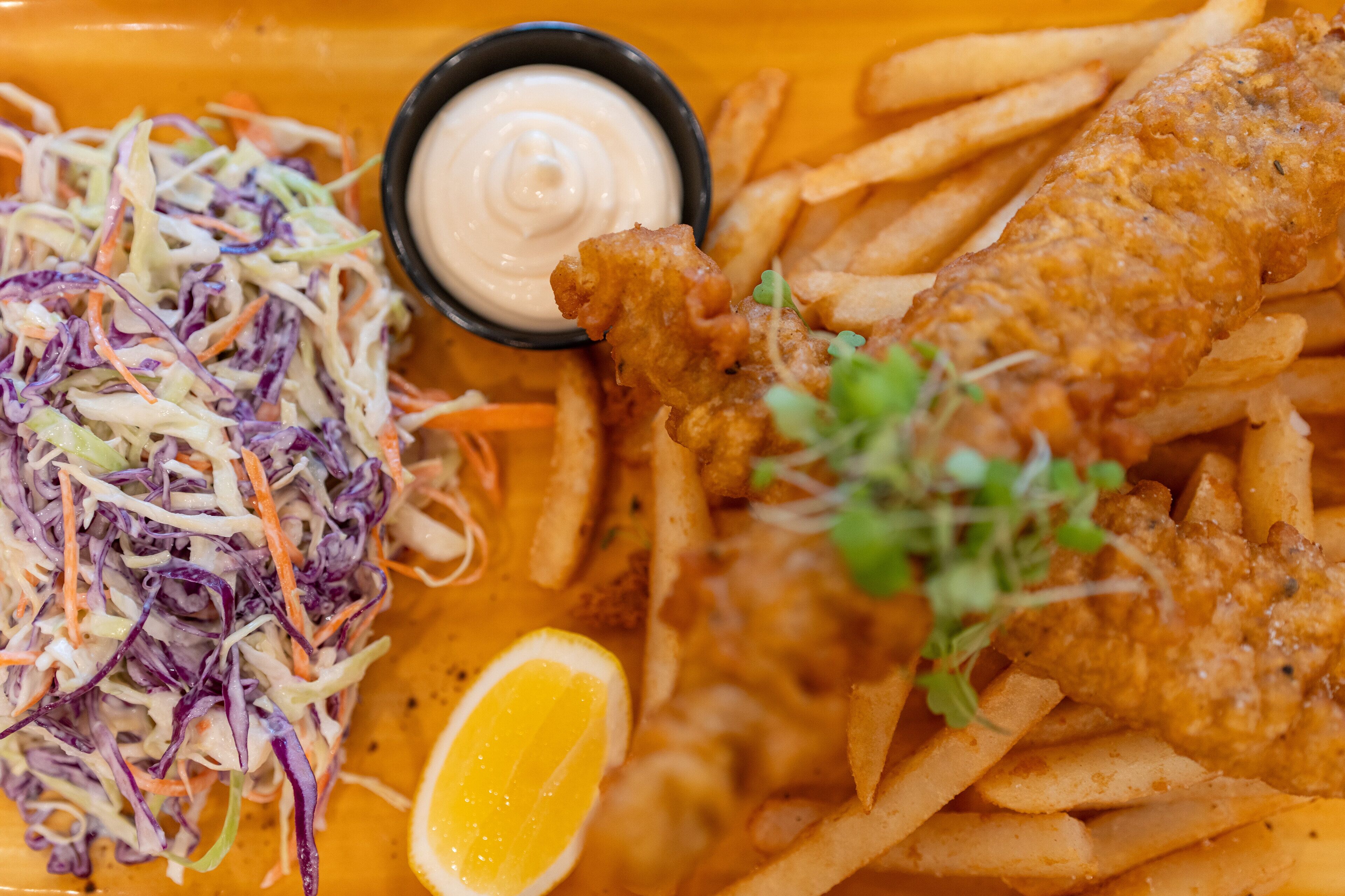 A plate of fish and chips with coleslaw and a lemon wedge.