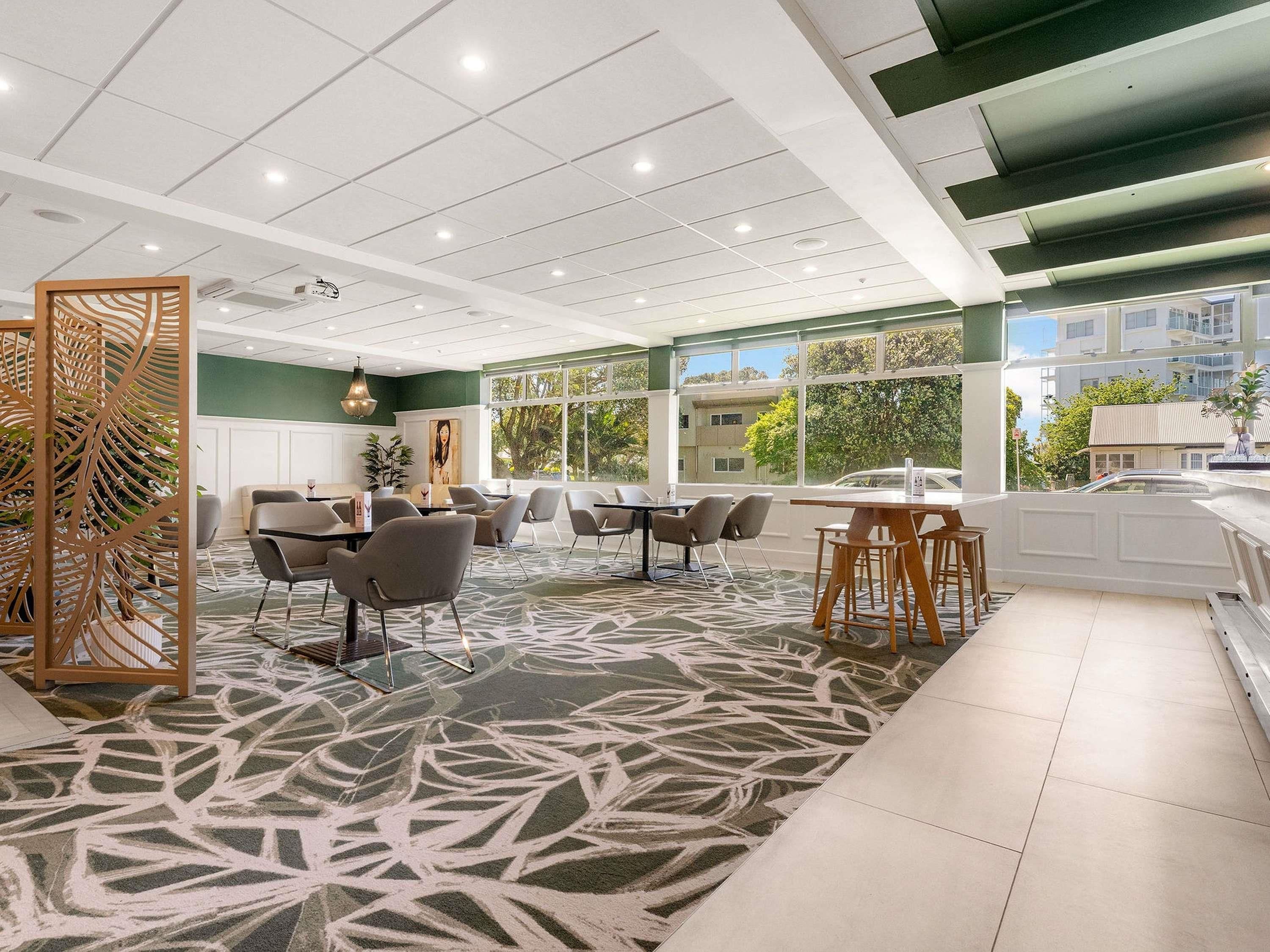 A modern hotel lobby with a large seating area, a reception desk, and large windows offering a view of the outdoors.