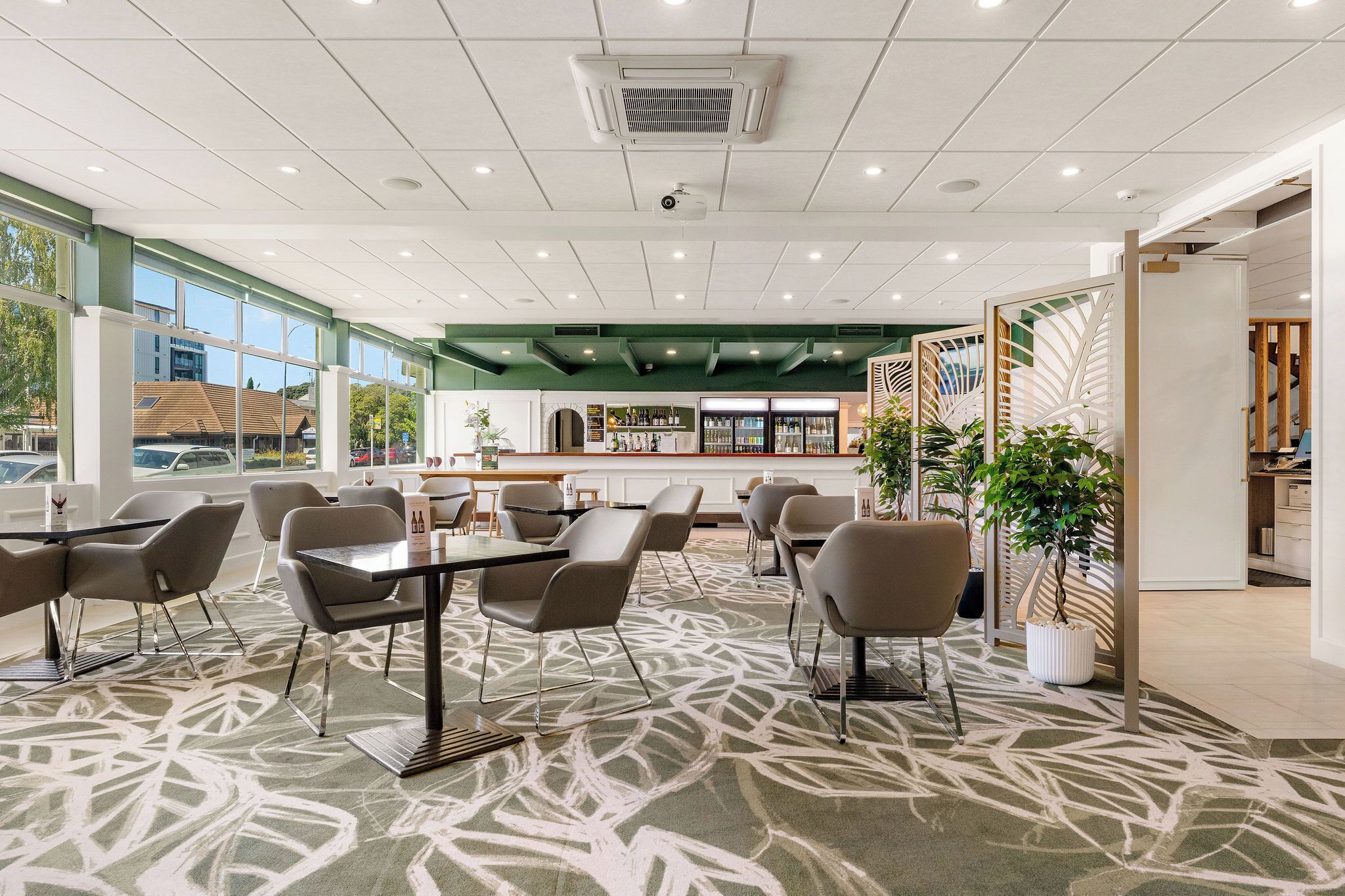 A spacious indoor area with tables and chairs, large windows, and a green accent wall.