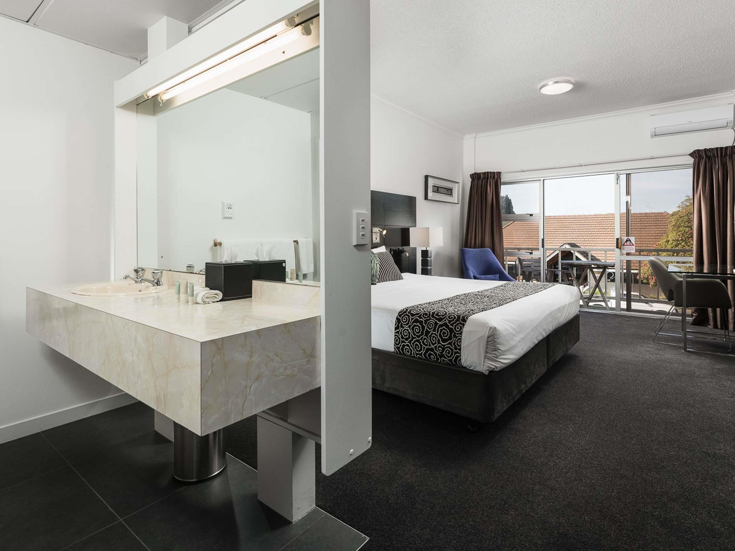 A hotel room with a bathroom, a bed, a desk, and a balcony.