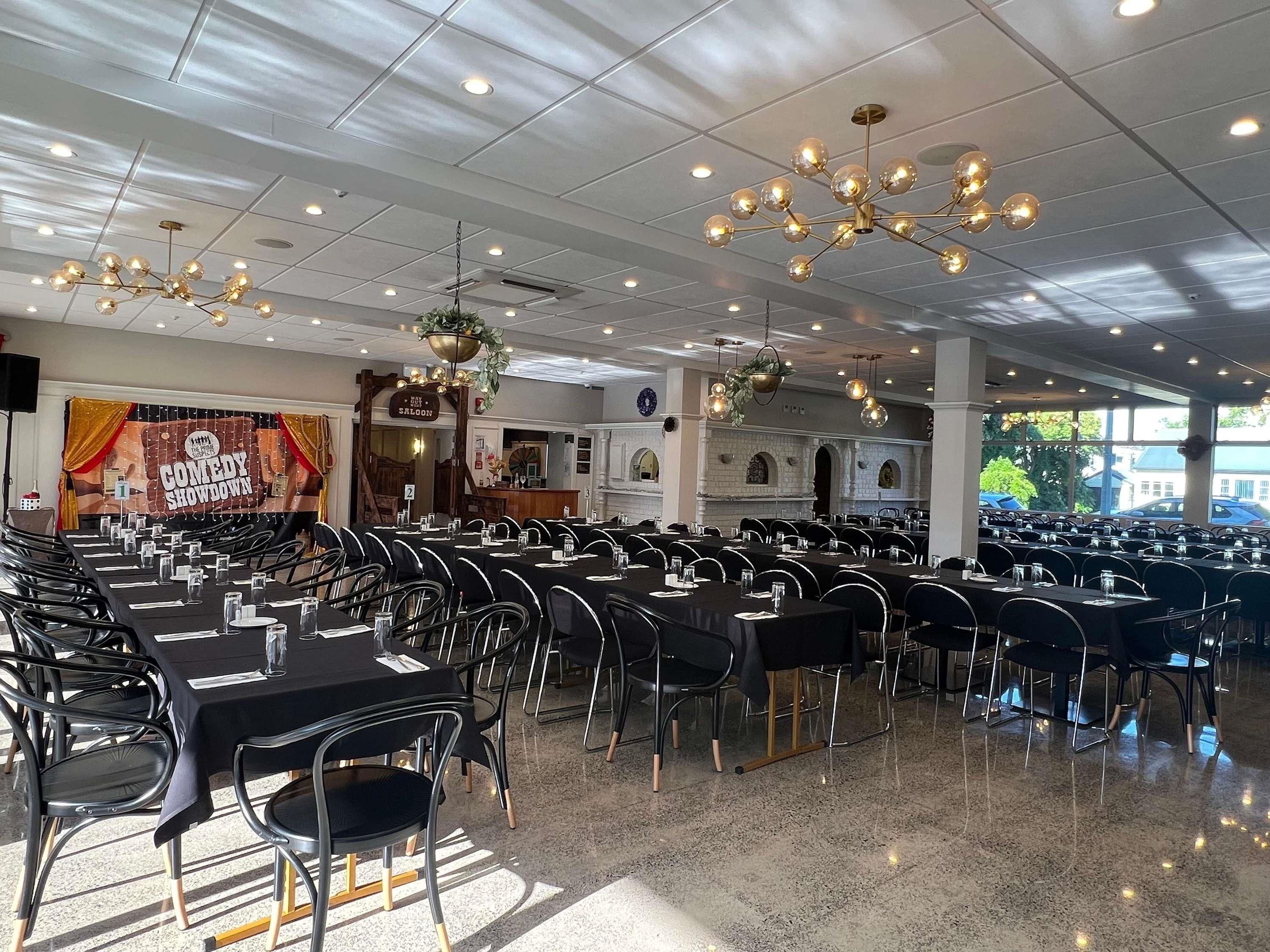 Un amplio comedor interior con varias mesas y sillas, luces en el techo y un cartel que anuncia un espectáculo de comedia.