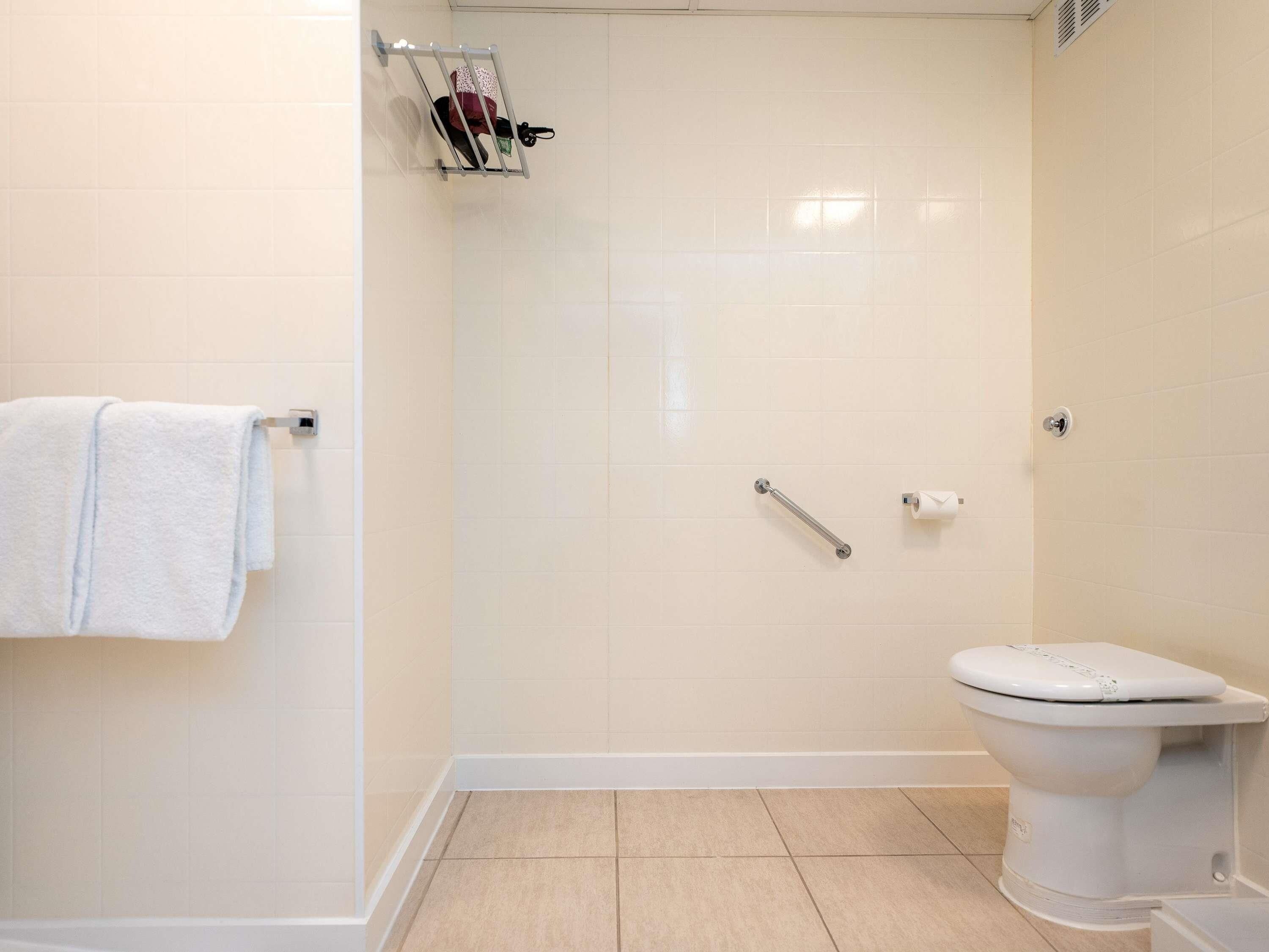 Une salle de bain avec des toilettes blanches, un espace douche et un porte-serviettes.