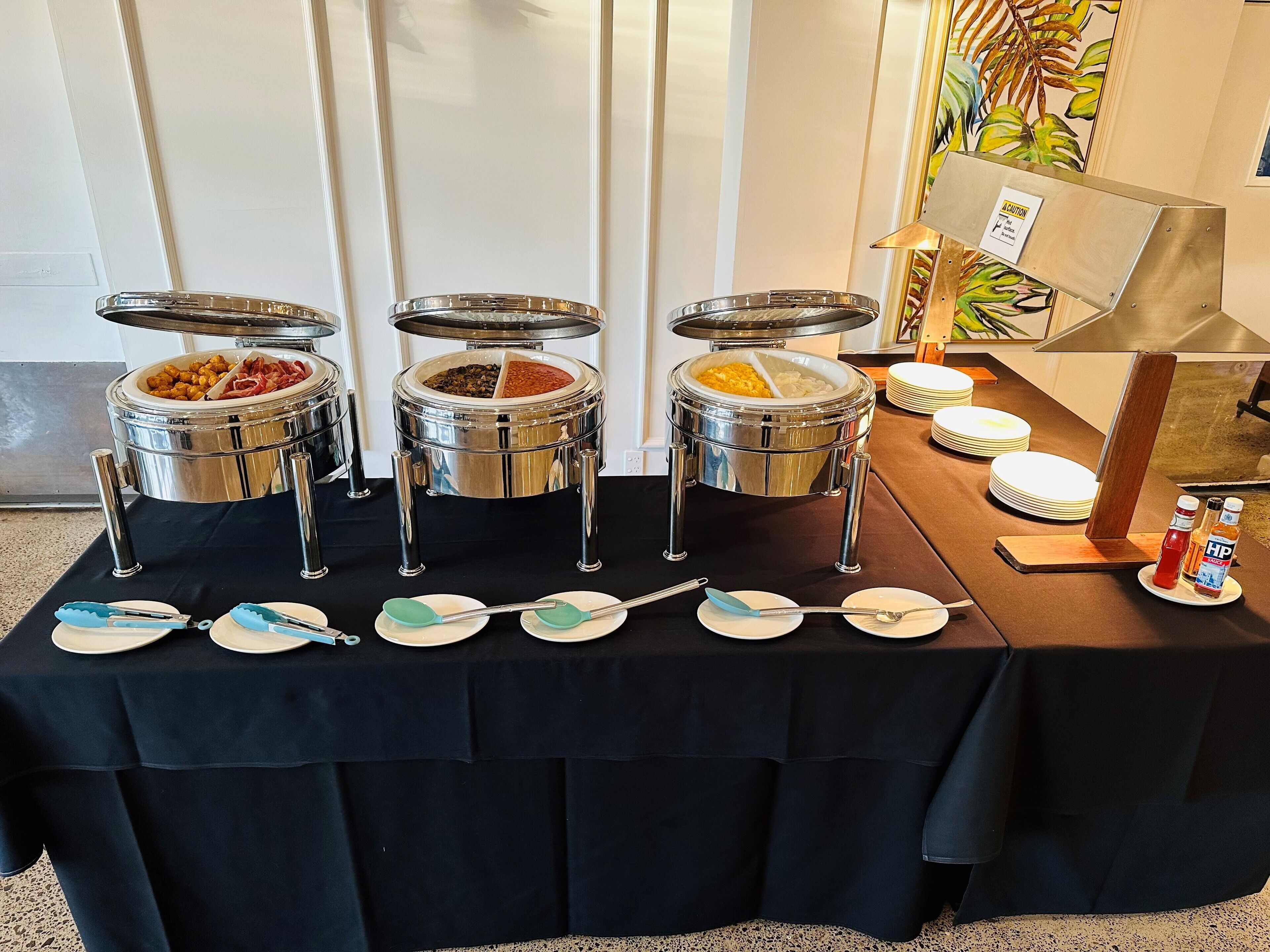 Una mesa de buffet con múltiples dispensadores de comida, platos y cubiertos.
