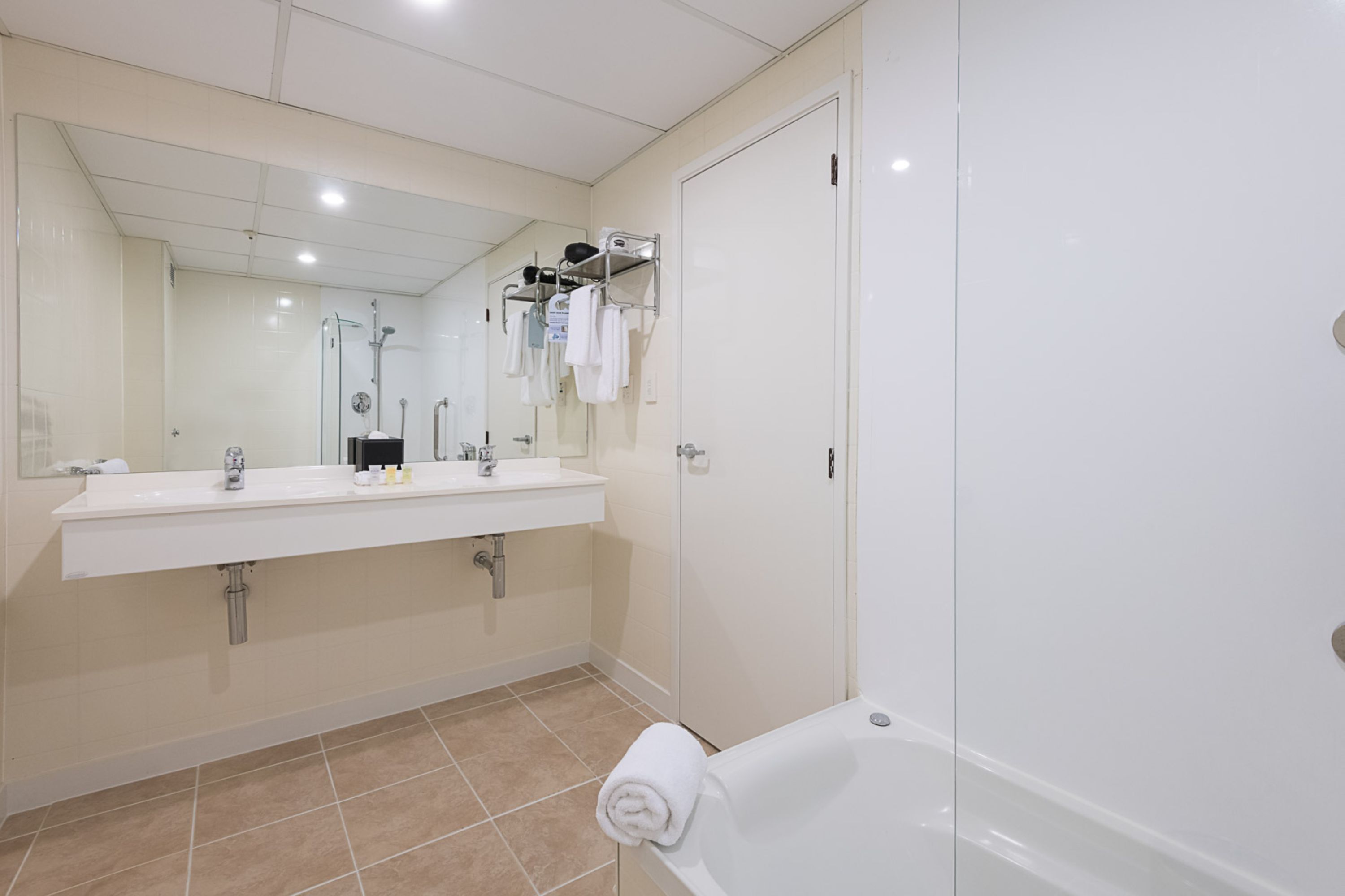 A modern bathroom with a large mirror, two sinks, a bathtub, and a shower.