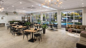 A spacious indoor area with multiple tables and chairs, a pool visible through large windows, and a variety of plants and decorative items. - Mercure Tauranga (Tauranga)