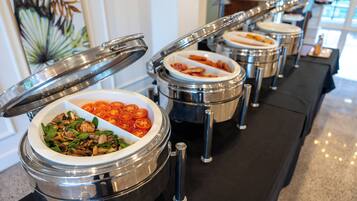Una barra de buffet con diversos alimentos en recipientes metálicos, cada uno con tapa.