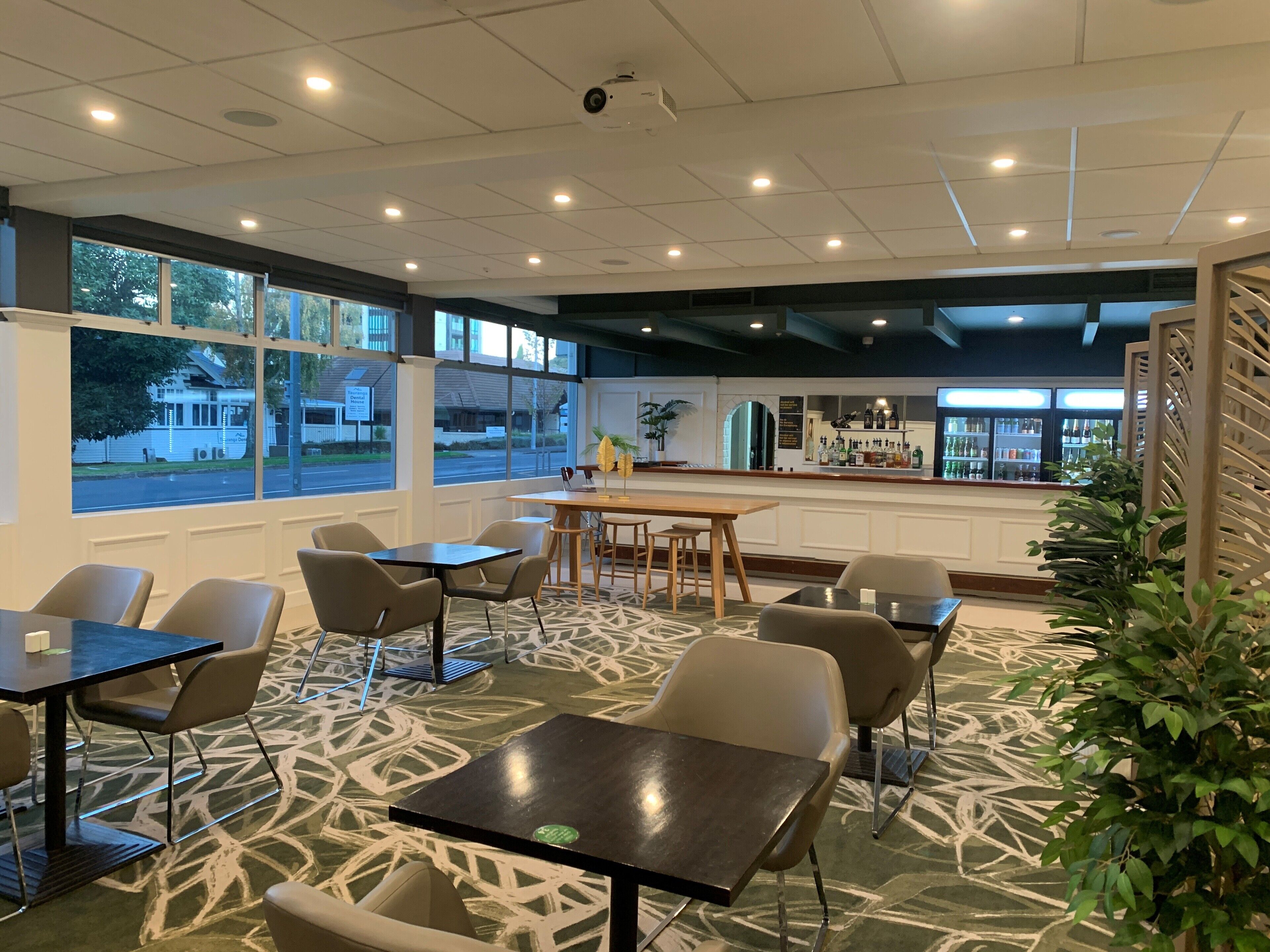 Un espace de restauration intérieur moderne, doté de nombreuses tables et chaises, de grandes fenêtres offrant une vue sur l’extérieur et d’un bar situé au fond de la pièce.