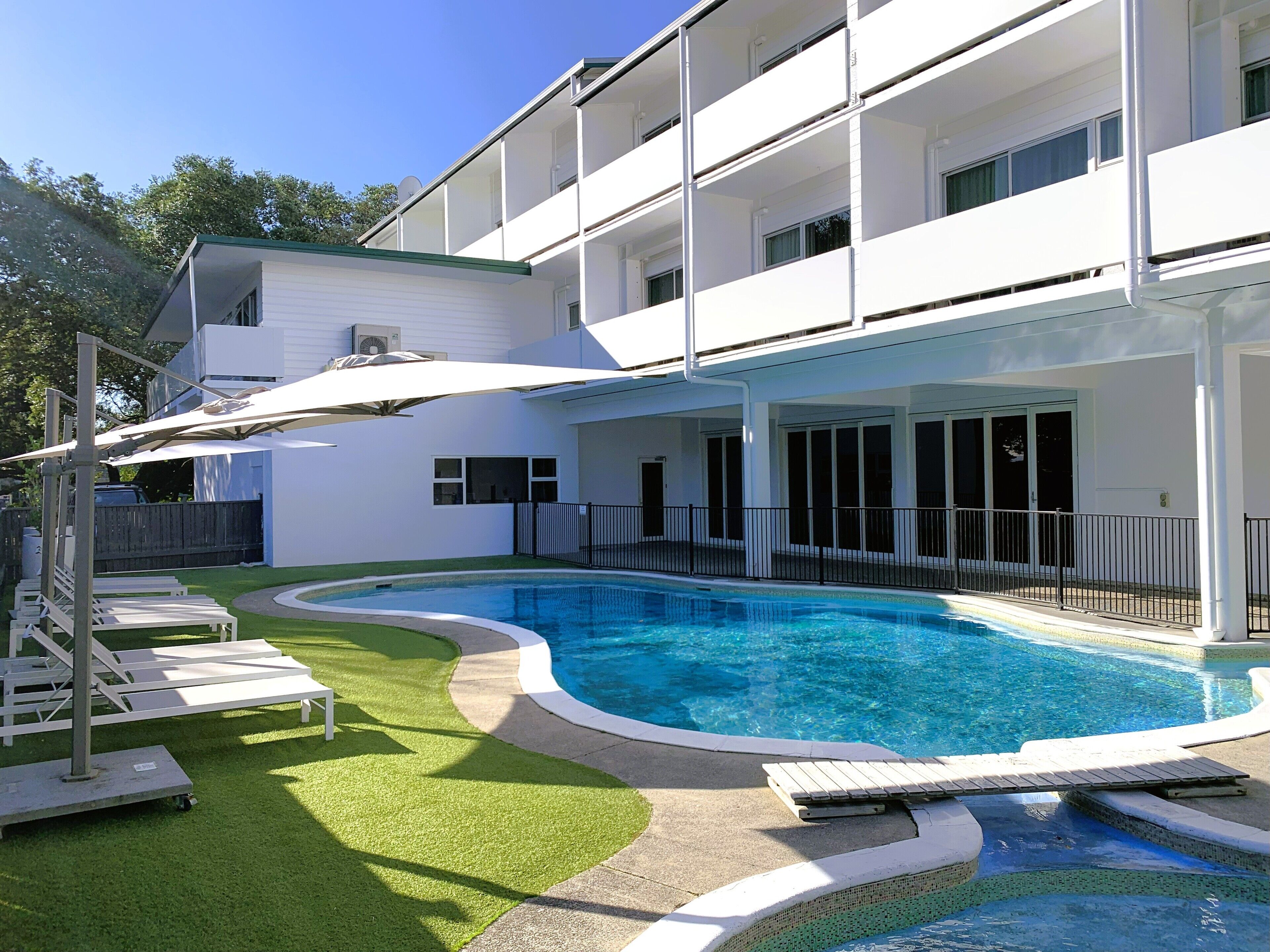 A modern two-story building with a swimming pool, outdoor lounge chairs, and a covered patio area.