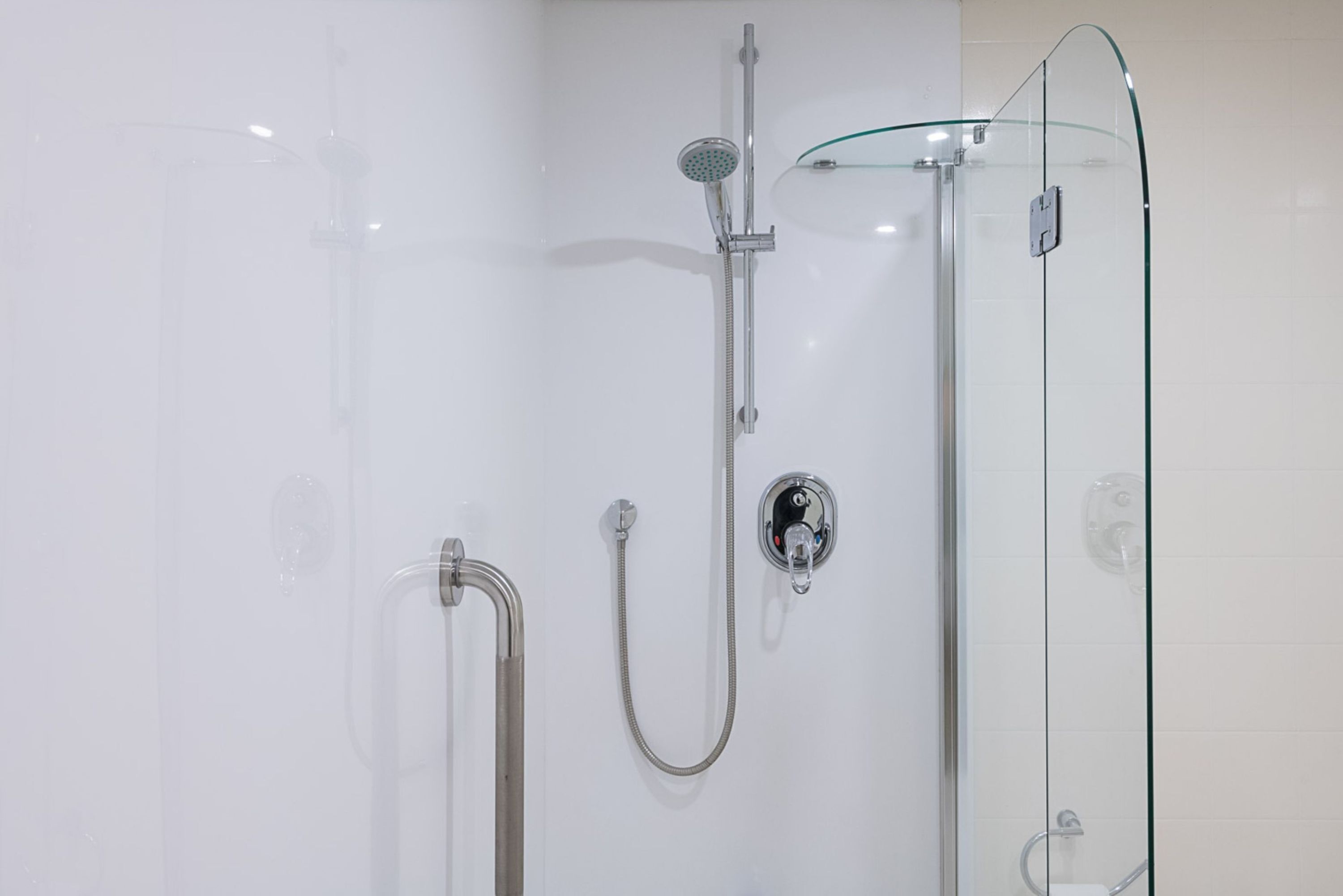 A glass-enclosed shower with a handheld showerhead and a wall-mounted control panel.
