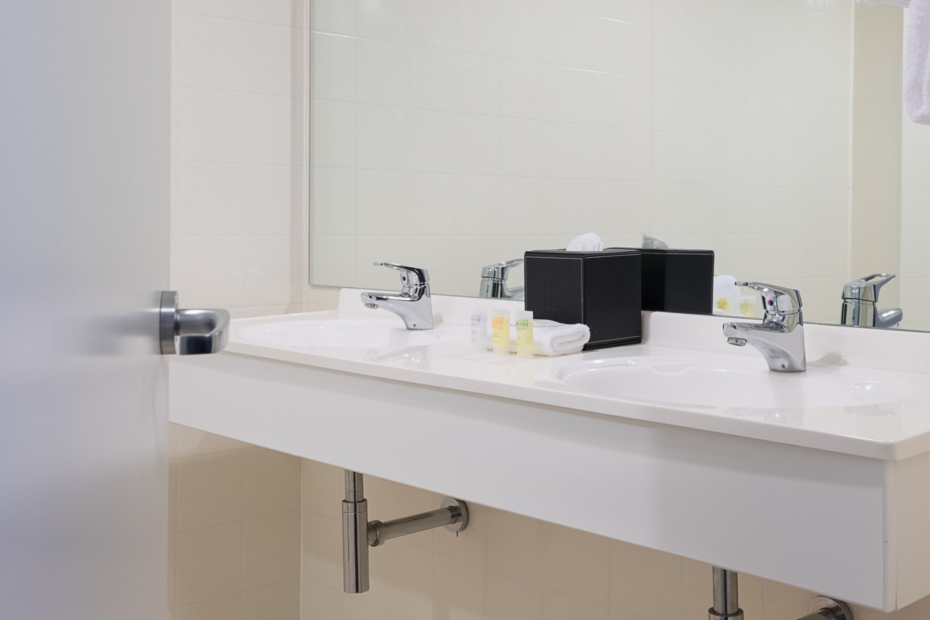 A modern bathroom with two sinks, a large mirror, and a towel rack.