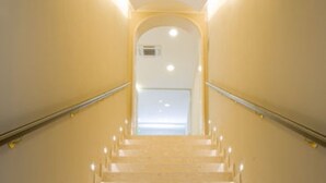 Uma escadaria de mármore com corrimãos, que leva a um patamar com uma porta e um candeeiro.