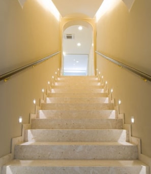 A marble staircase with handrails, leading to a landing with a door and a light fixture.