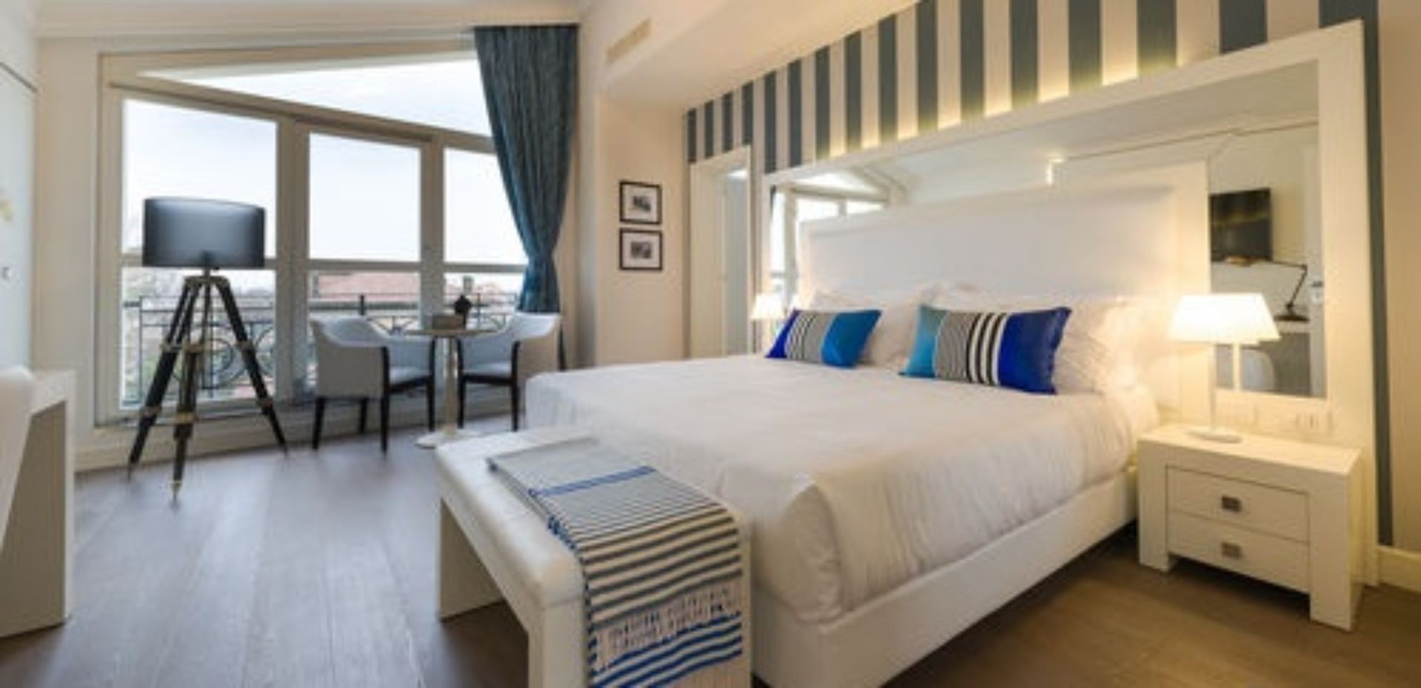Habitación de hotel con una cama grande, un escritorio con silla, un balcón con vistas y una ventana con cortinas.