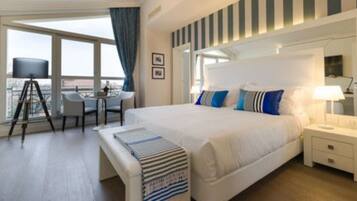 Habitación de hotel con una cama grande, un escritorio con silla, un balcón con vistas y una ventana con cortinas.