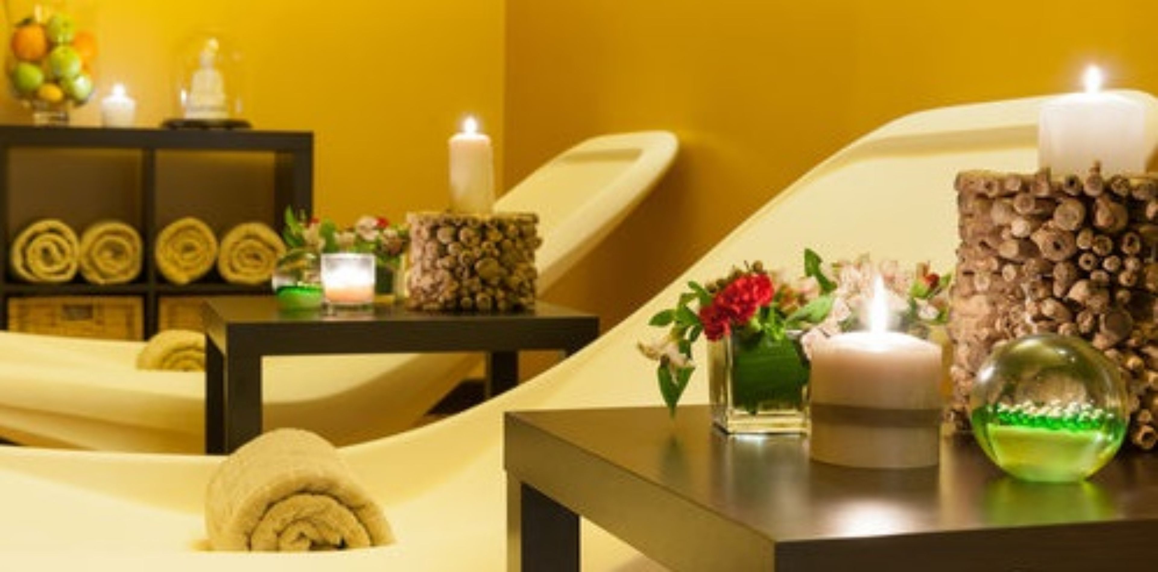 Un cuarto de spa con una camilla de masaje, velas y un florero decorativo con flores.