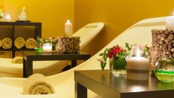 Un cuarto de spa con una camilla de masaje, velas y un florero decorativo con flores.