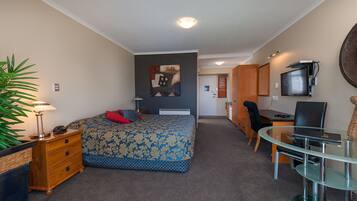 Habitación de hotel con cama, escritorio, silla, lámpara, televisión y planta.