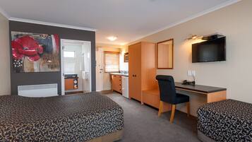A hotel room with two beds, a desk, a chair, a TV, and a kitchen area.
