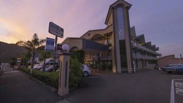 A hotel entrance with a modern design, a parking area, and a signboard.