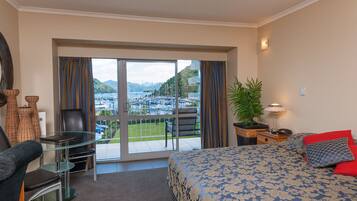 Une chambre d’hôtel équipée d’un lit, d’un bureau, d’une chaise, d’une plante en pot et offrant une vue sur un port de plaisance.