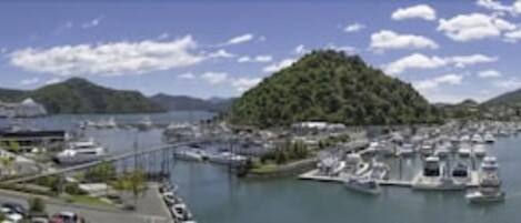 A marina with boats docked, a bridge, and a mountainous backdrop.