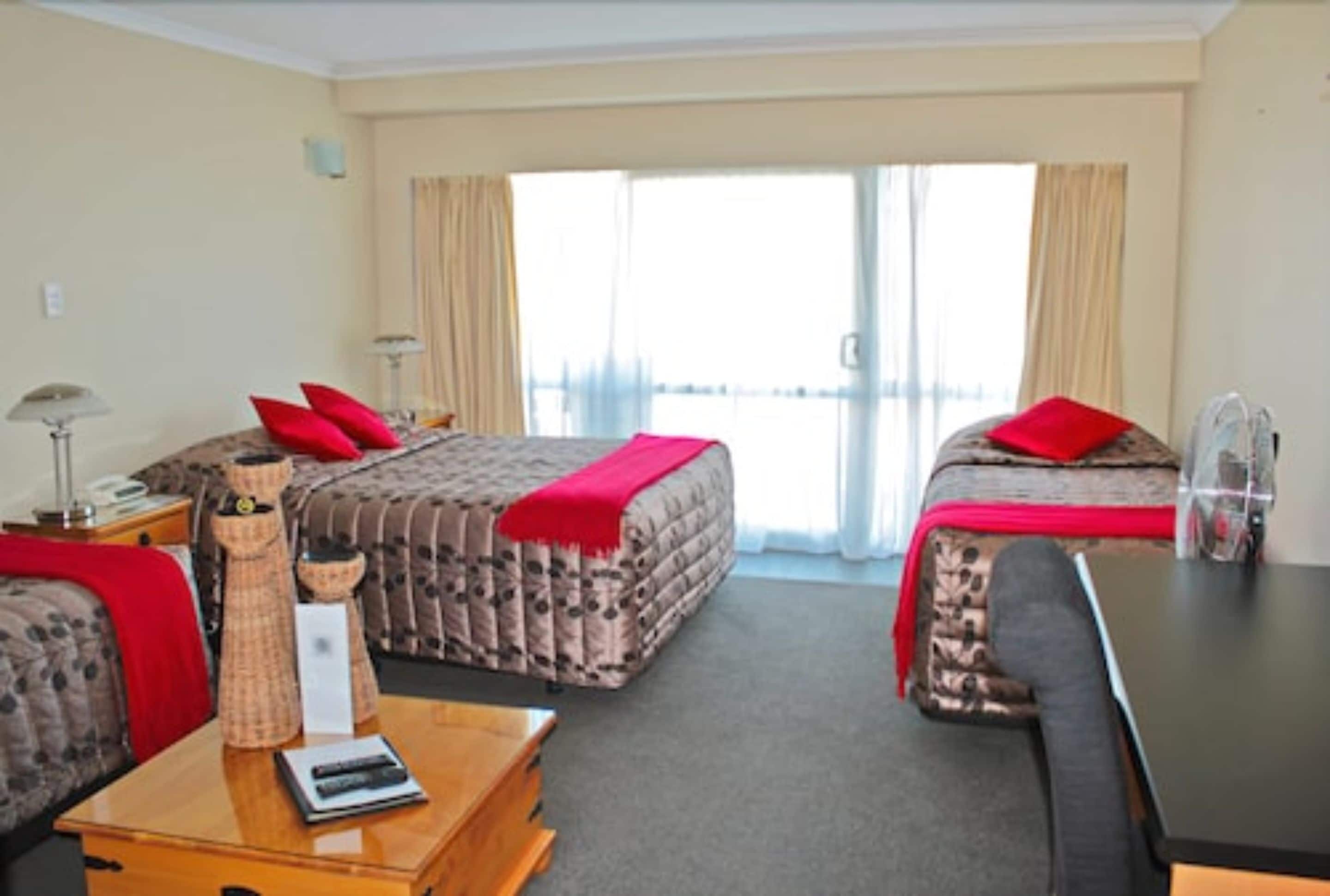 A hotel room with two beds, a desk, a chair, and a large window with curtains.
