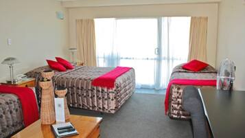 A hotel room with two beds, a desk, a chair, and a large window with curtains.