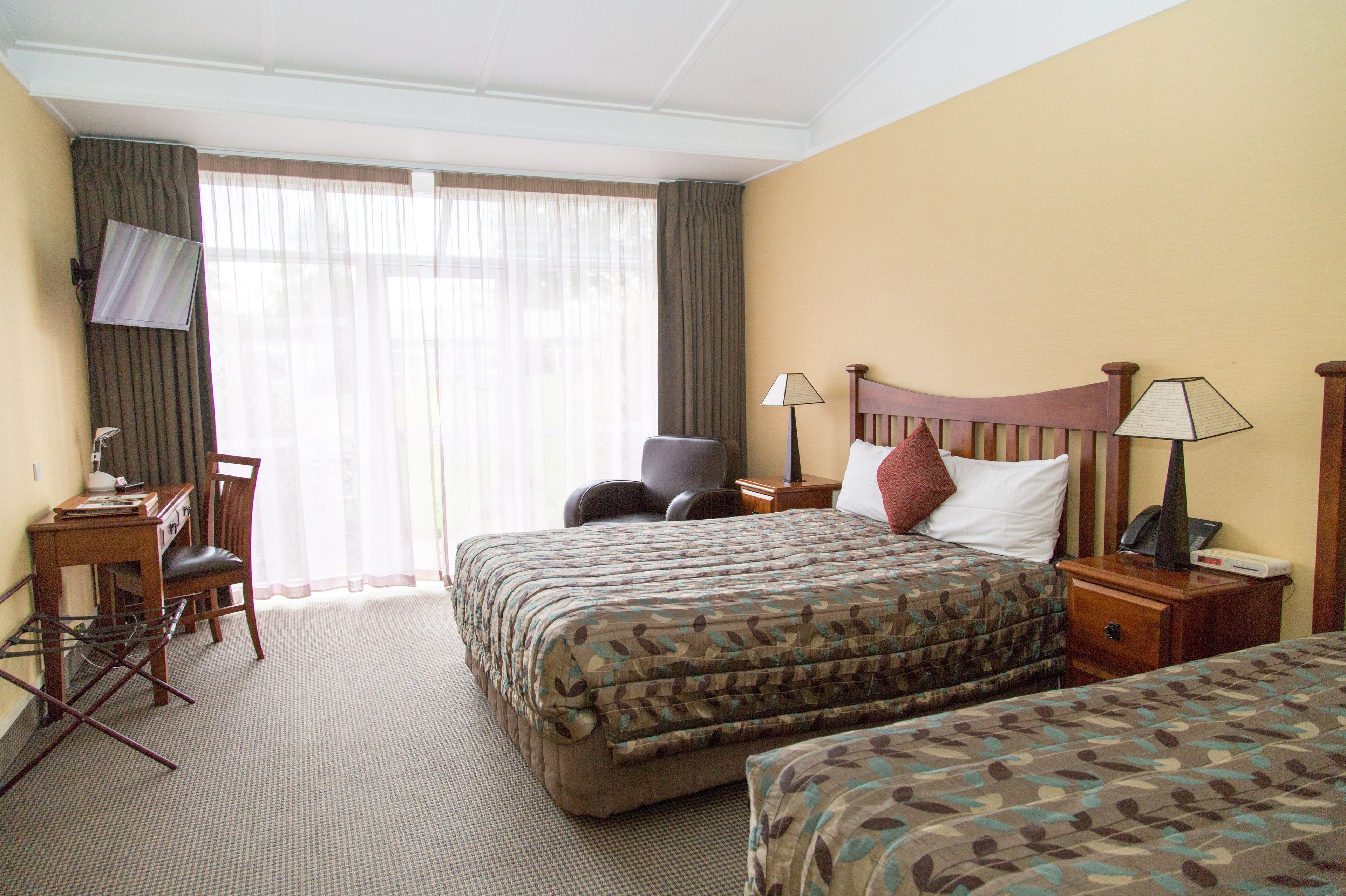 Une chambre d’hôtel avec un grand lit, un bureau avec une chaise, un téléviseur fixé au mur et une fenêtre avec des rideaux.