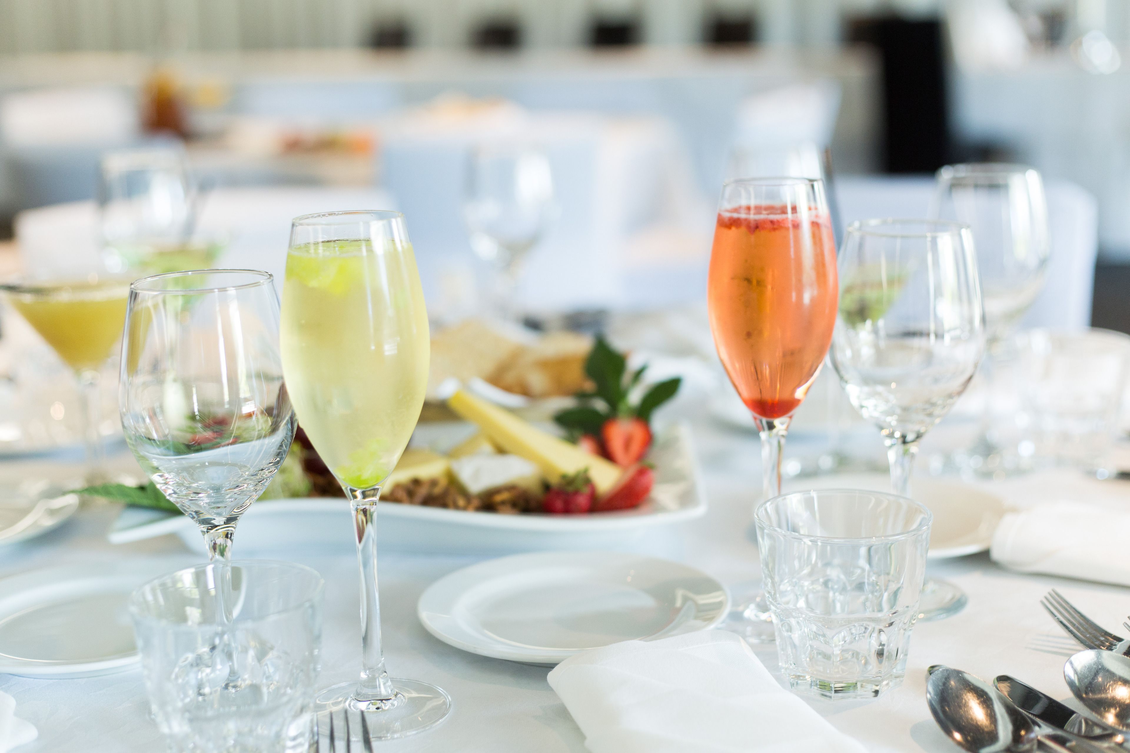 A table set for a meal with multiple glasses of beverages, plates with food, and cutlery.
