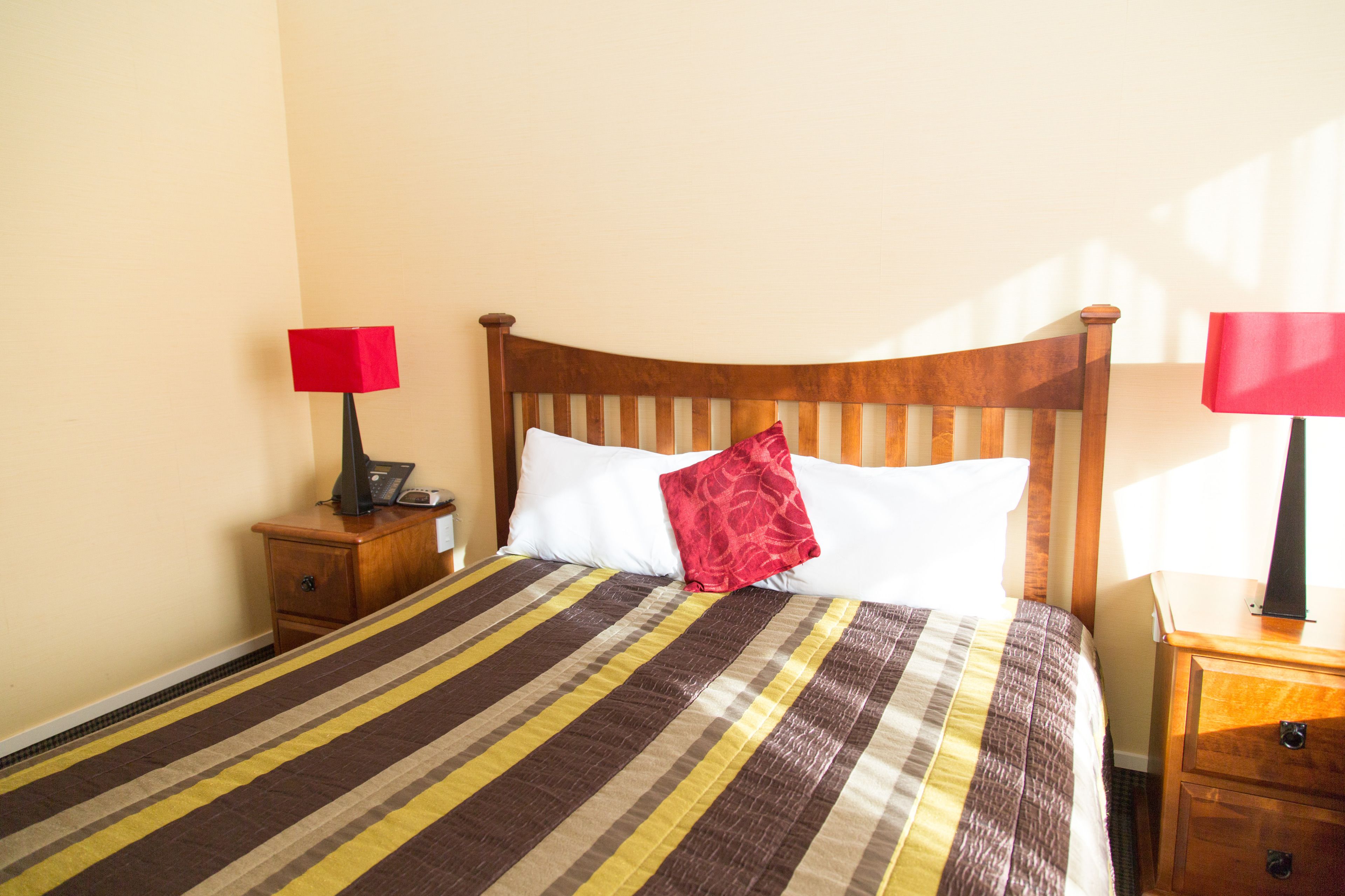 Cama bem arrumada com colcha listrada, duas mesas de cabeceira com abajures e cabeceira de madeira.