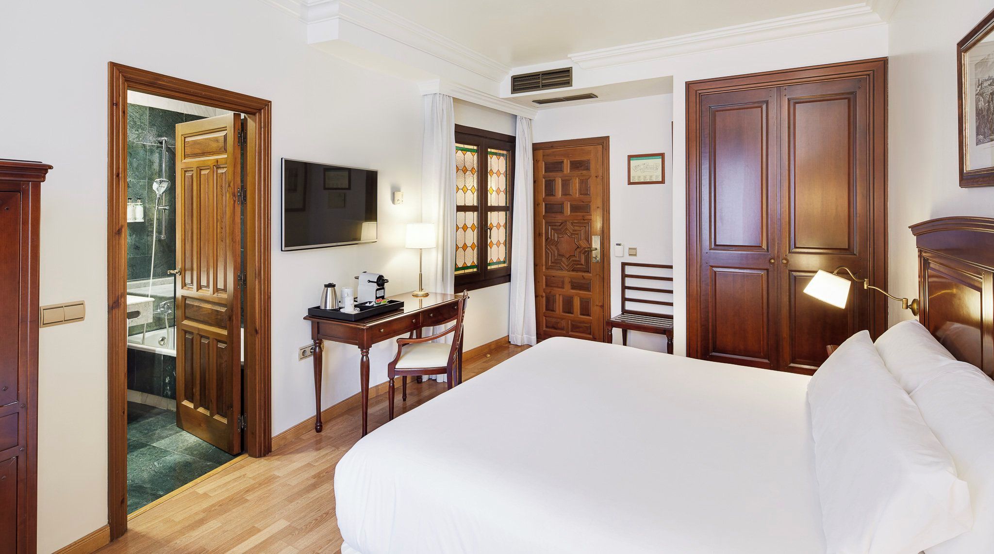Una habitación de hotel con una cama grande, un escritorio con silla, un televisor y una ventana con cortinas.