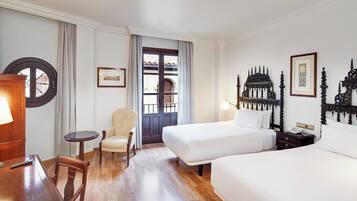 A hotel room with a bed, a chair, a small table, and a desk with a lamp.