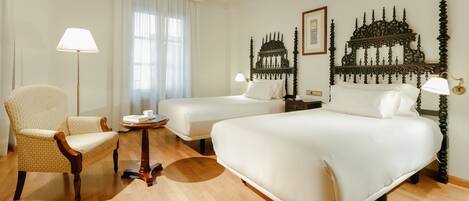 A hotel room with a large bed, two smaller beds, a chair, a table, and decorative headboards.