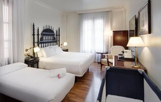 A hotel room with two beds, a desk, a chair, a lamp, and a decorative wall piece.