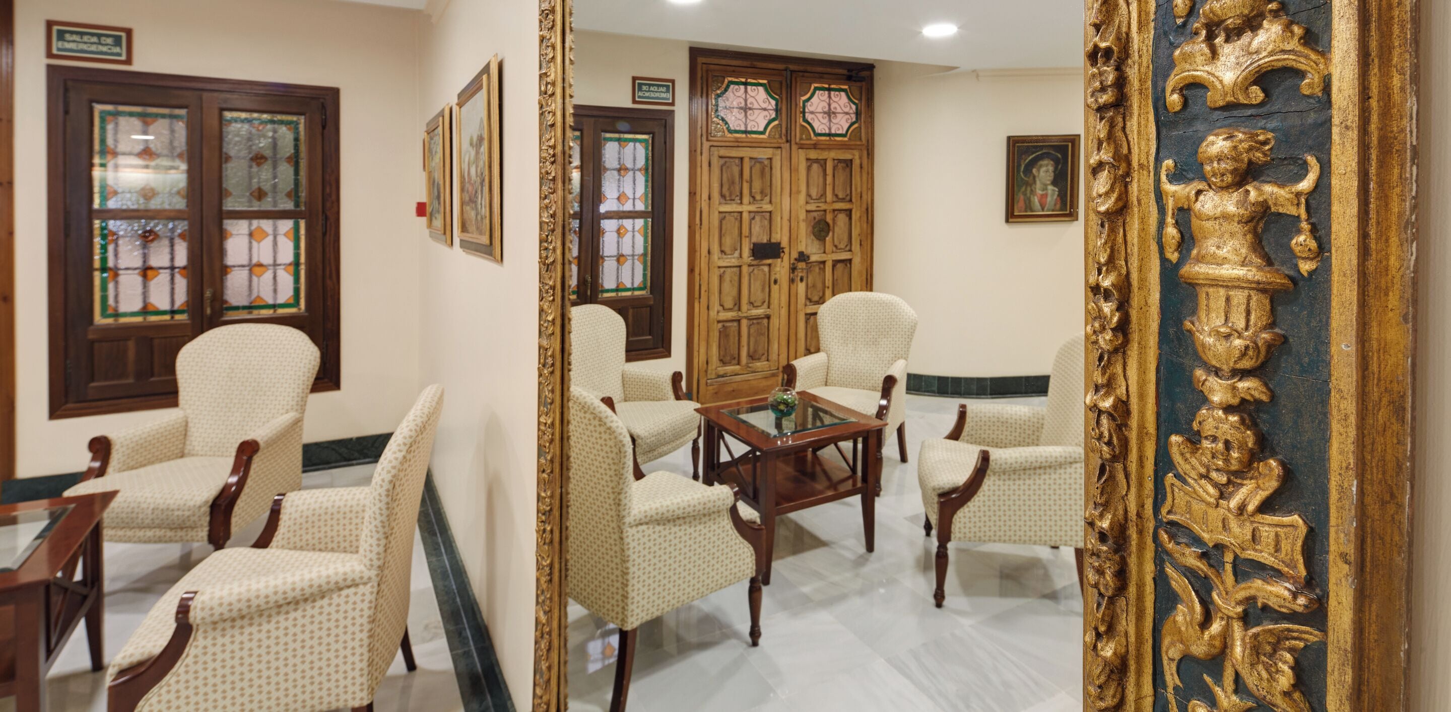 A room with a wooden door, a glass door, and a mirror with a golden frame.