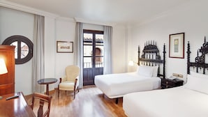 Ein Hotelzimmer mit Bett, Stuhl, Schreibtisch, Lampe und einem fenster mit Vorhängen.
